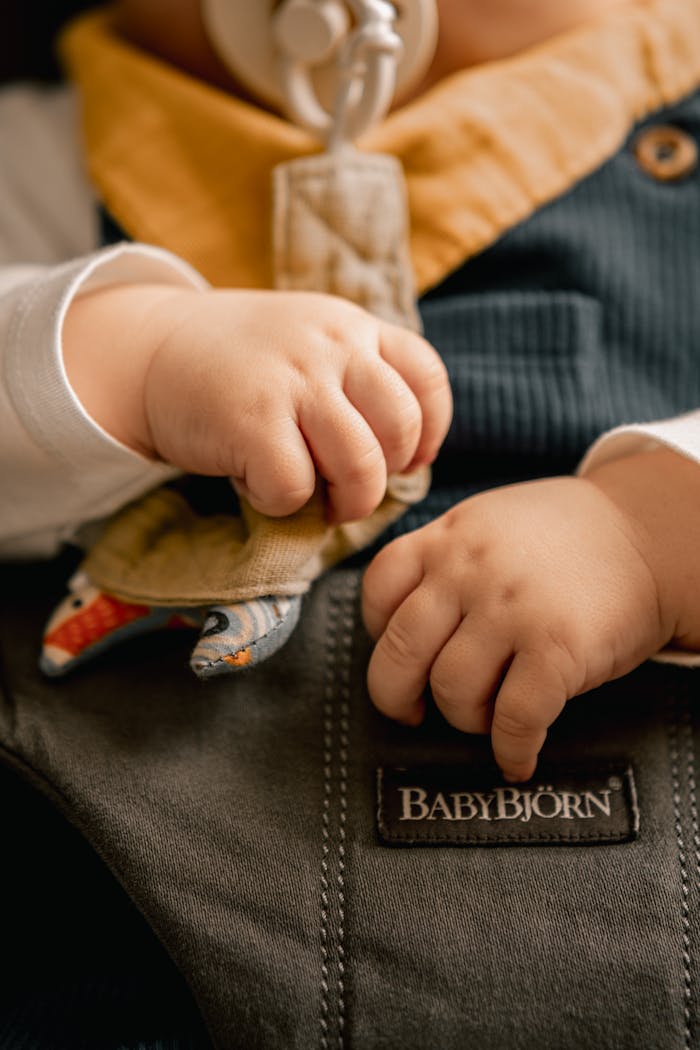 Adorable close-up of a baby's hands gripping a BabyBjörn carrier, showing warmth and comfort.